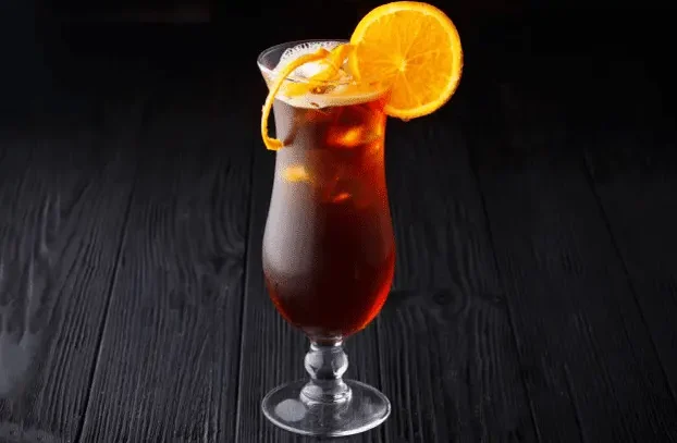 Long Island Iced Tea servido en copa alta con rodaja de naranja sobre barra oscura